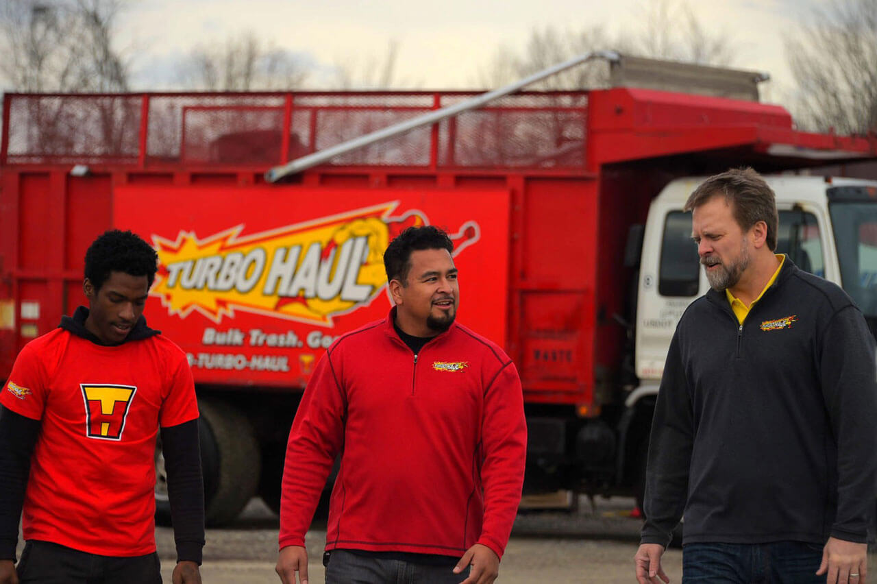 CEO of TurboHaul walk with two employees from their junk removal trucks in Severn, Maryland.