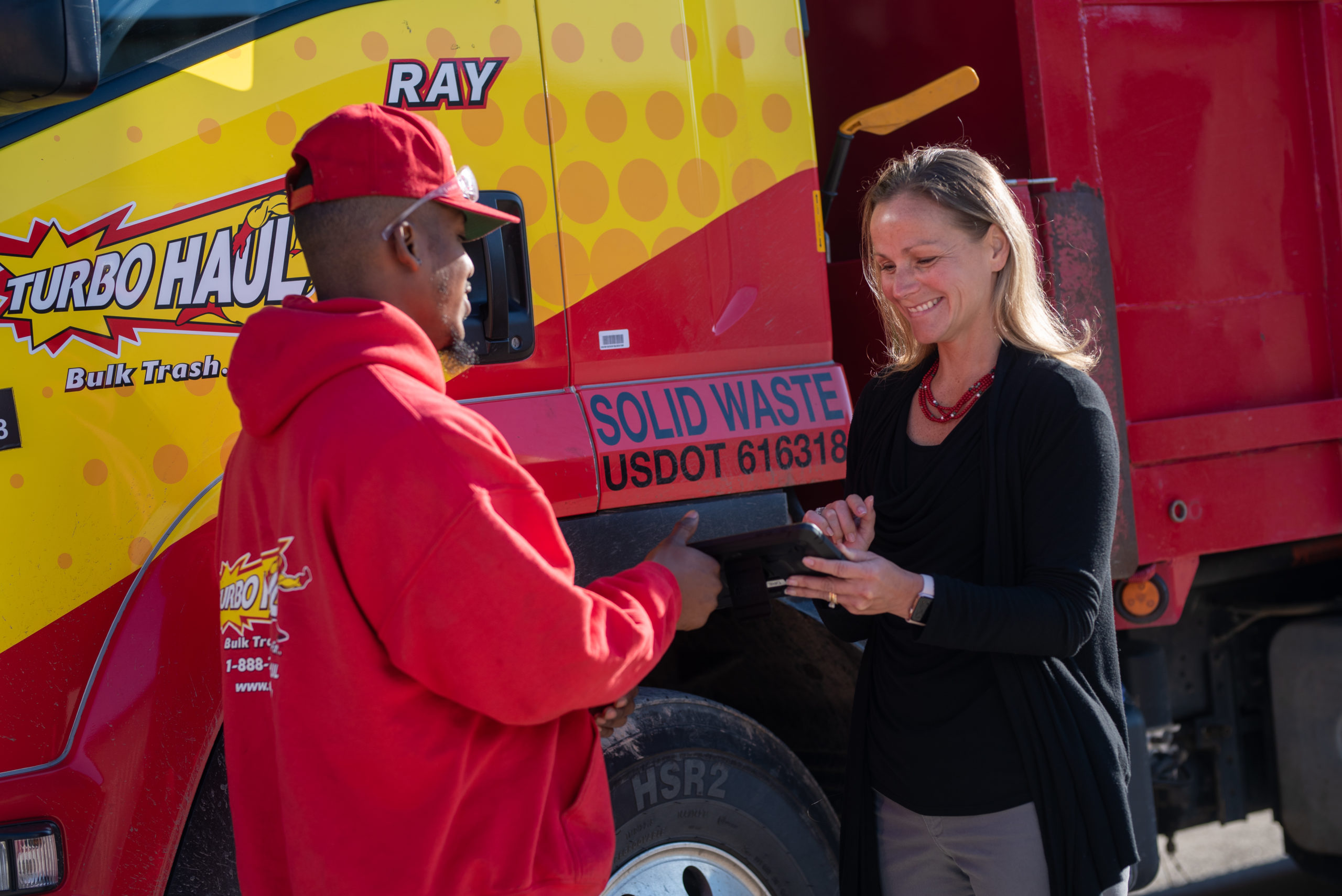 A junk removal specialist hands a tablet to another TurboHaul employee in Lisbon, MD